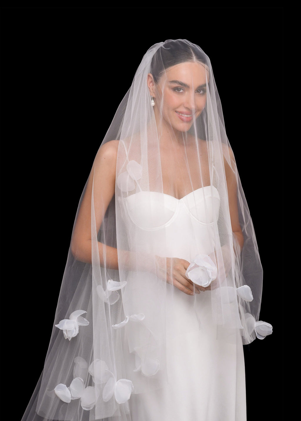 Bride wearing a white wedding dress with a floral veil against a black background