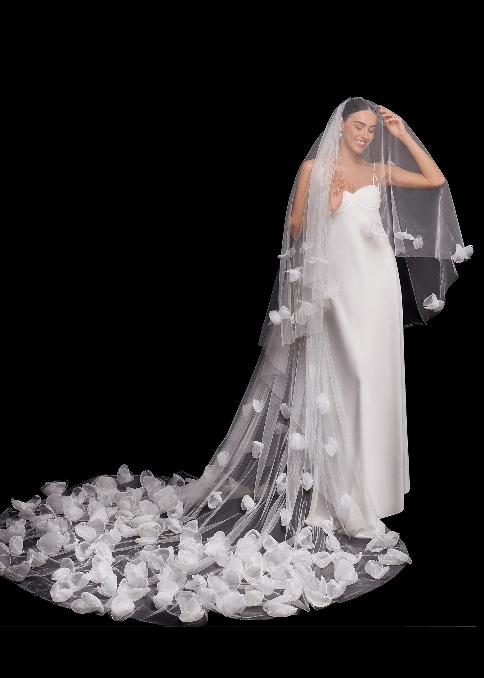 Bride wearing a long, elegant wedding veil with floral details on a black background