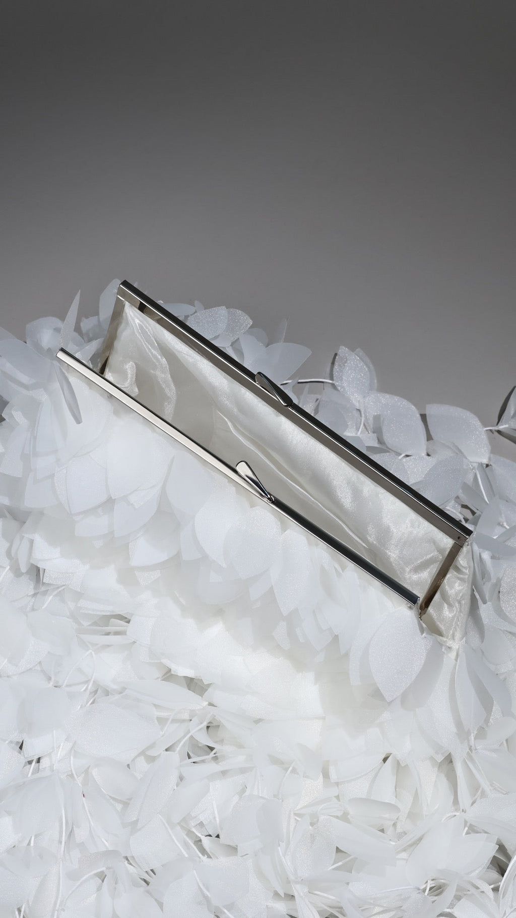 Silver clutch on a bed of white feathers with a gray background