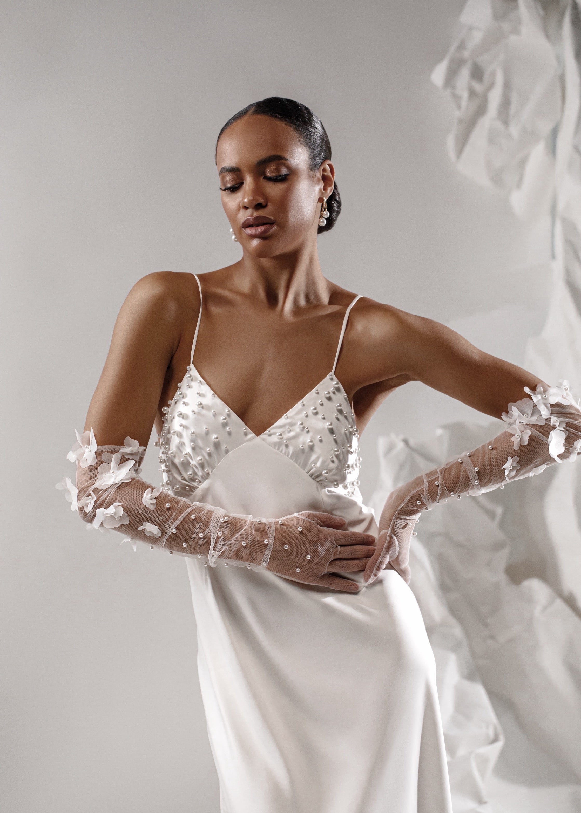 Woman in a white wedding dress with lace gloves against a neutral background