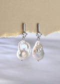 Pearl earrings with silver hooks on a textured beige and white background