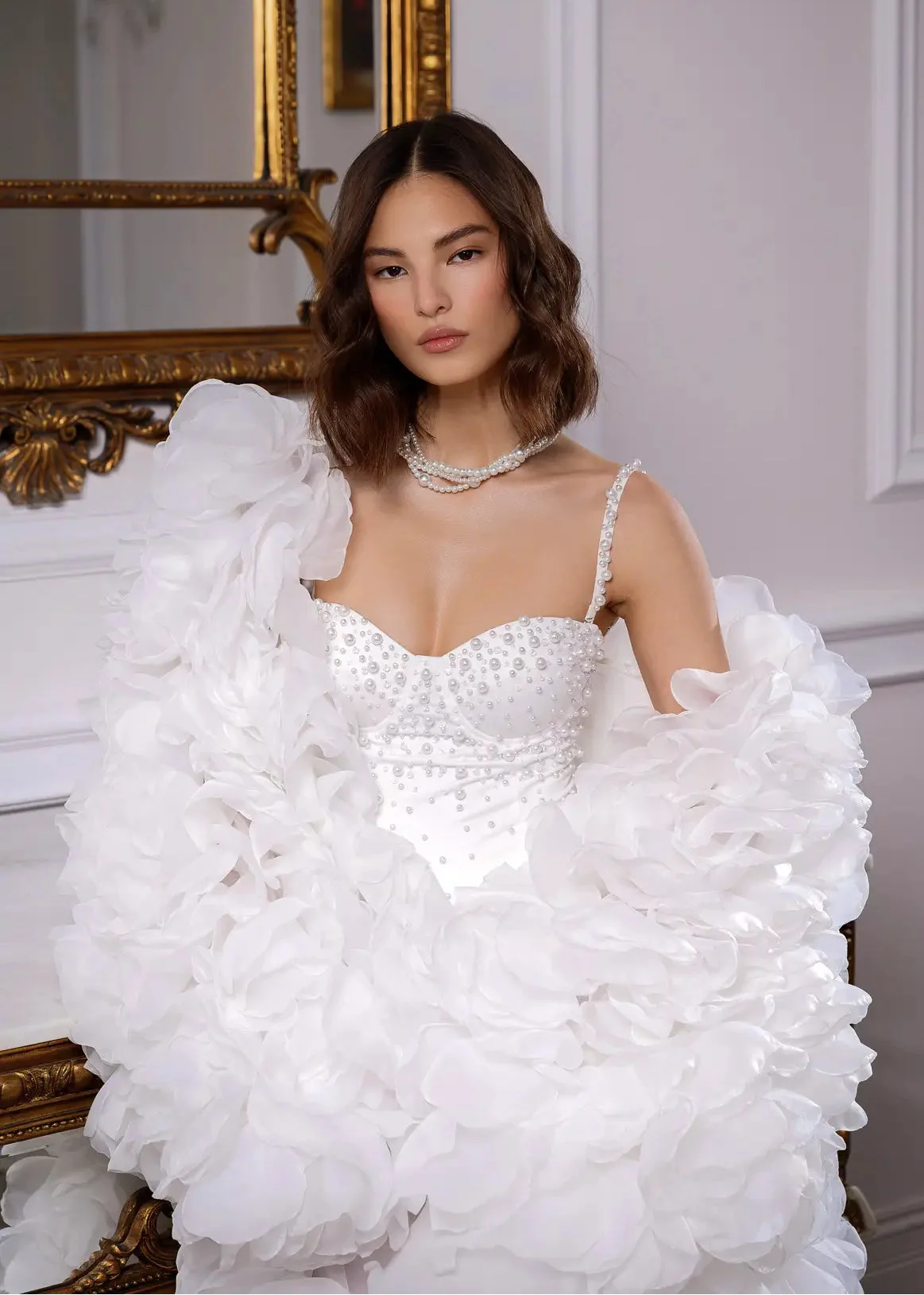 Woman wearing a white wedding dress with ruffled sleeves in an elegant interior setting.