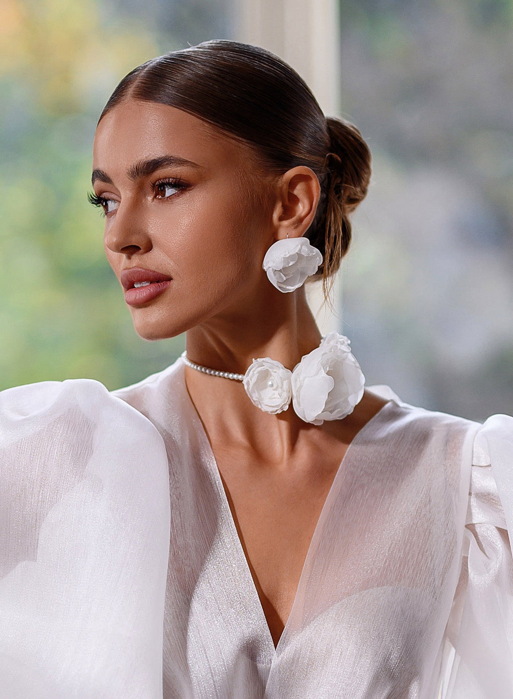 Woman wearing large white floral earrings and a white outfit with a blurred natural background