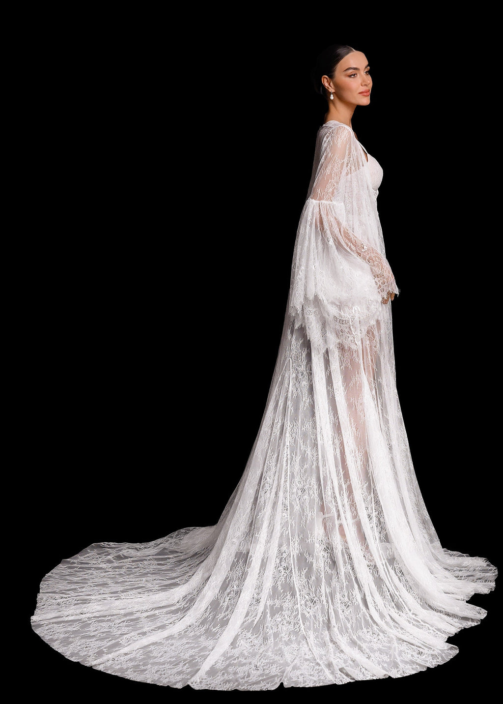 Woman wearing a long, elegant white lace dress with a flowing train on a black background