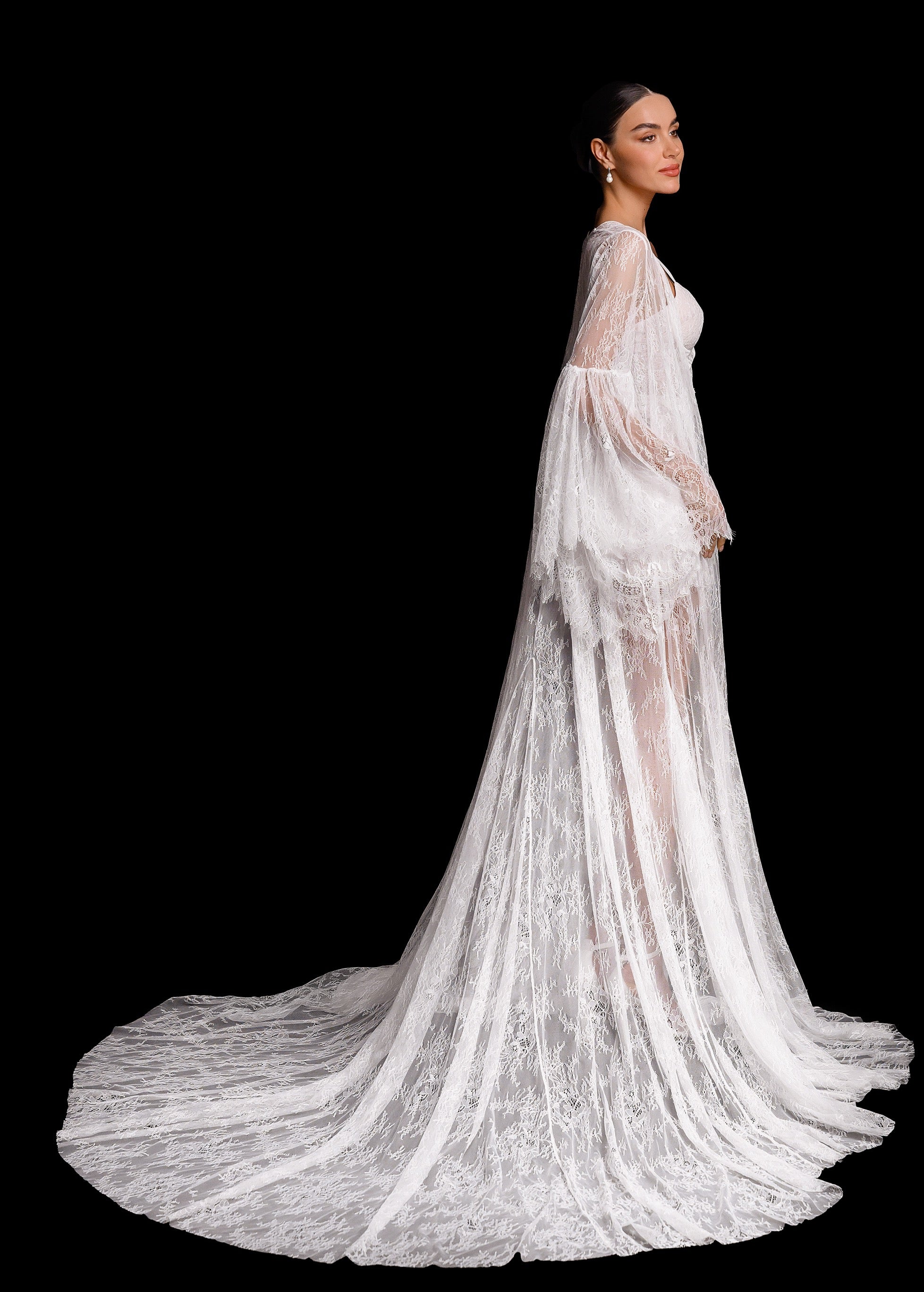 Woman wearing a long, elegant white lace dress with a flowing train on a black background