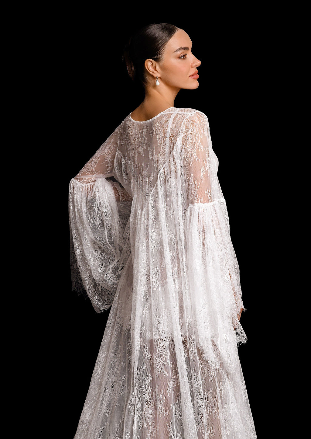 Woman wearing a sheer, embroidered white dress against a black background