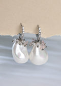 Pearl earrings with silver and pink accents on a light blue and beige background