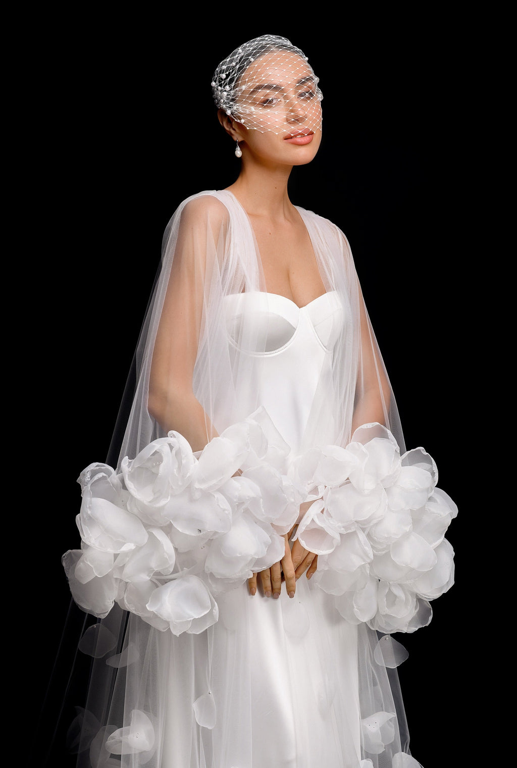 Woman in a white wedding dress holding a large white bouquet against a black background