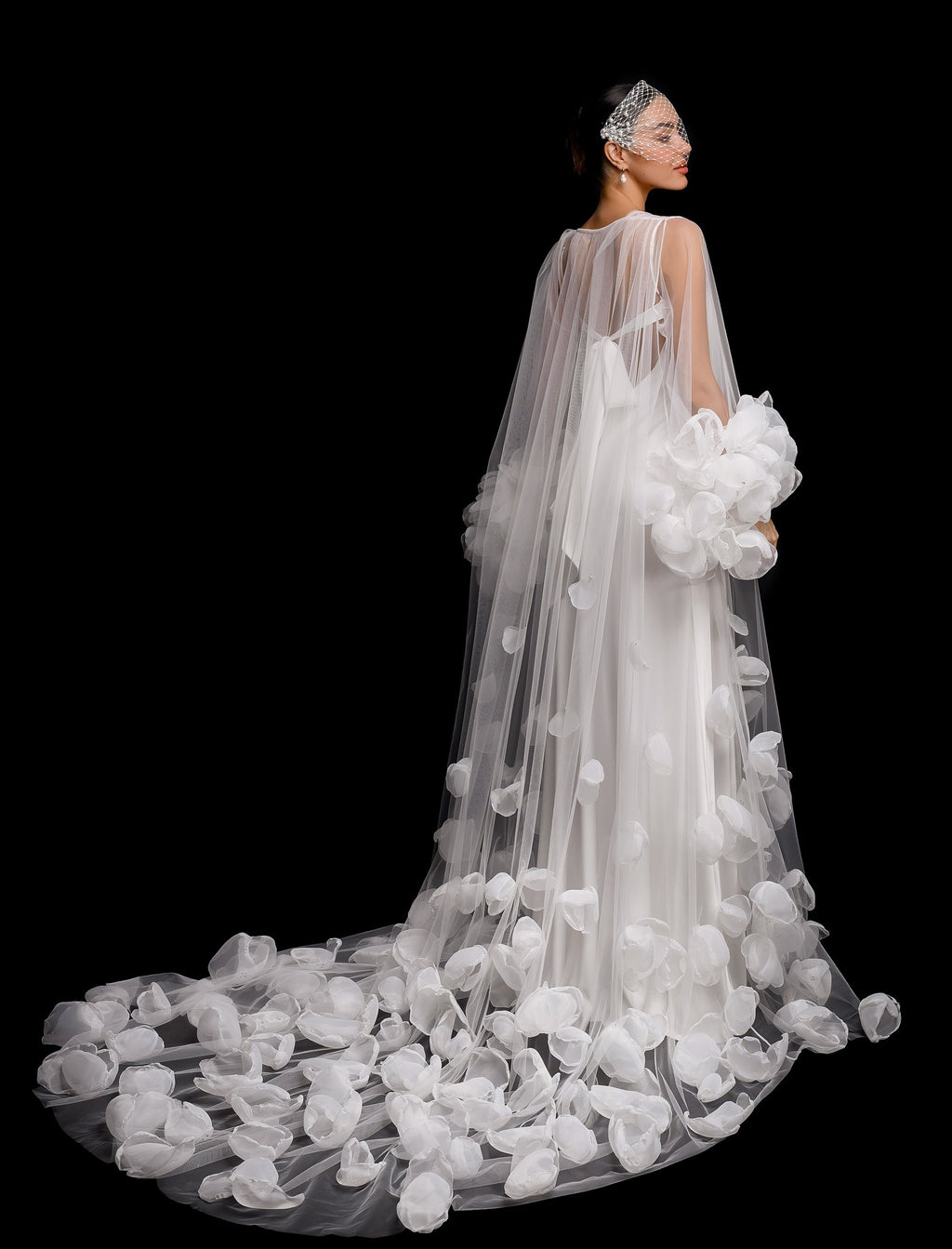 Bride in a white wedding gown with a long train and floral details against a black background