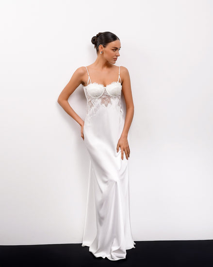 Woman wearing a white satin slip dress against a plain background