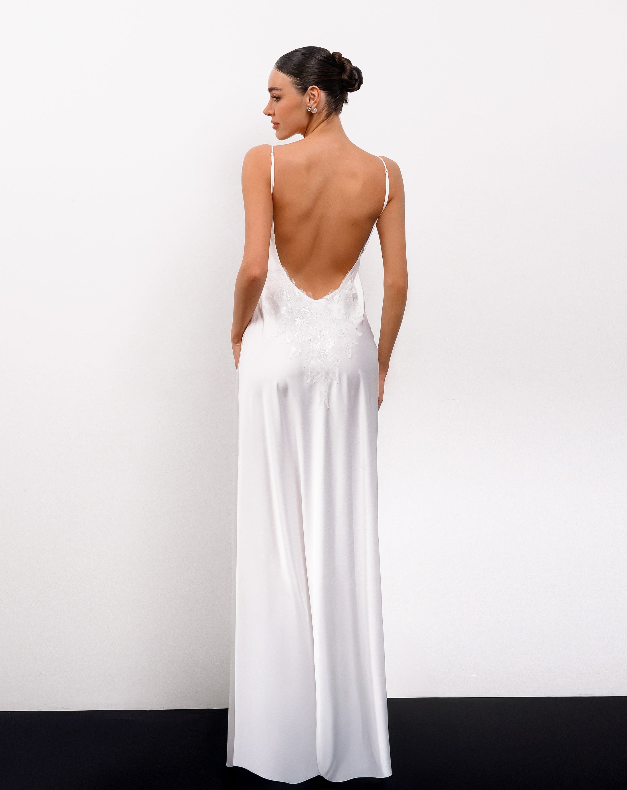 Woman wearing a white dress with a low back design against a plain background
