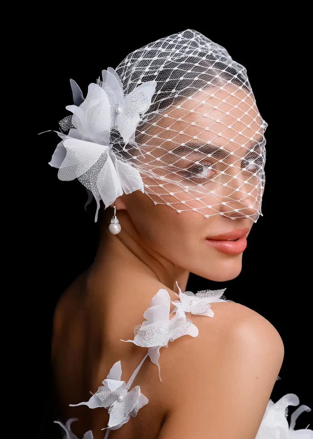 Woman wearing a birdcage veil with white flowers against a black background