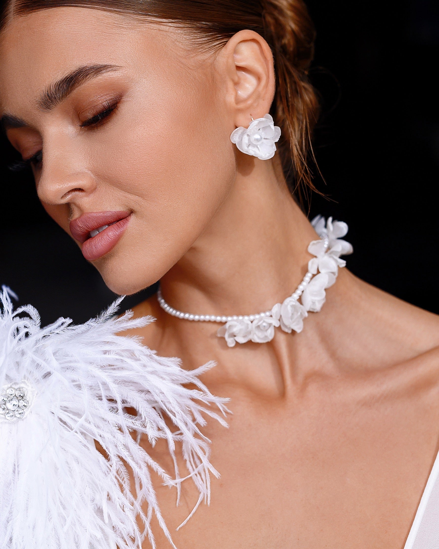 Woman wearing white floral earrings and a matching necklace with a black background