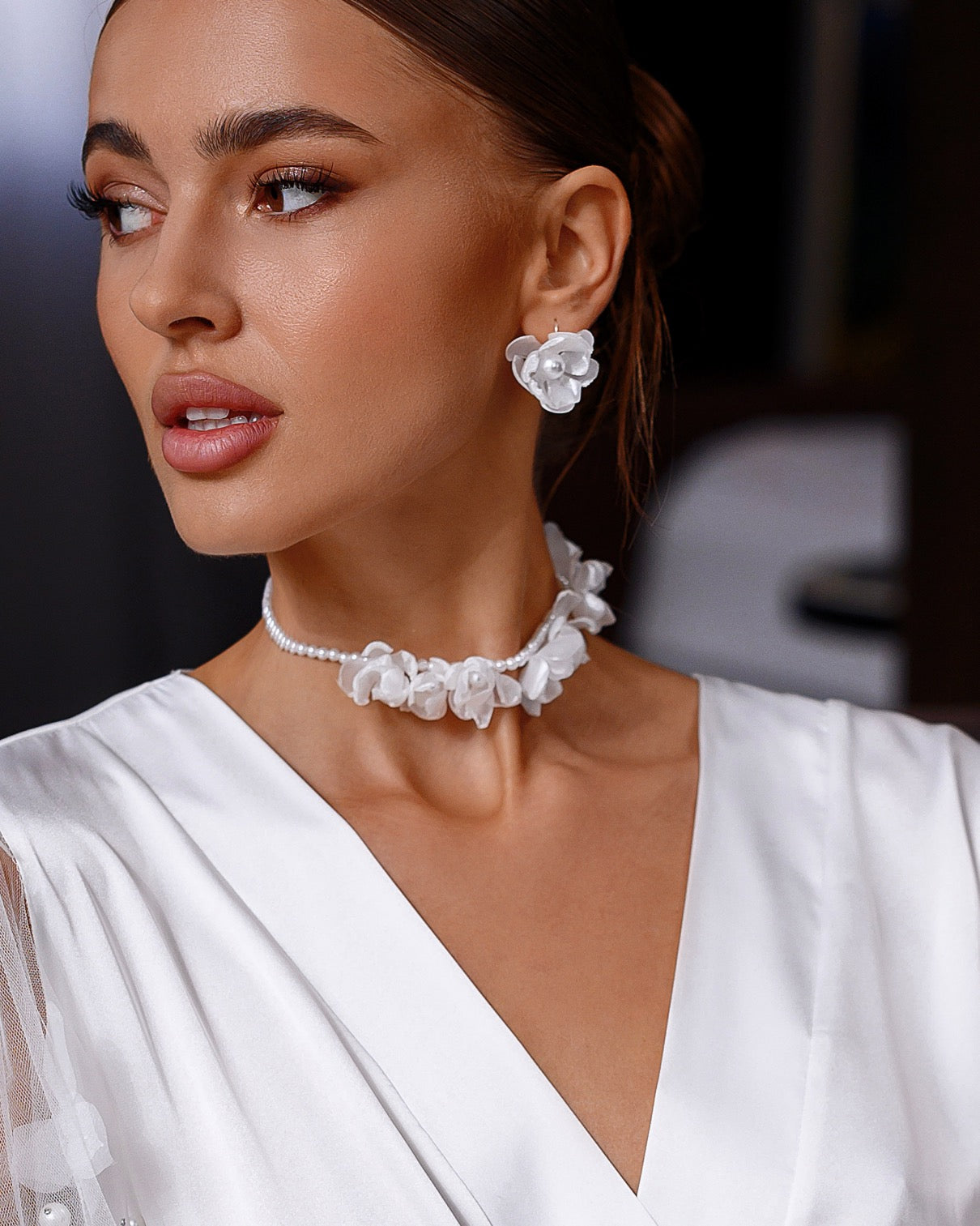 Woman wearing a white dress with floral jewelry against a blurred background